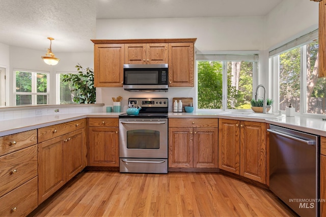 kitchen with appliances with stainless steel finishes, a sink, light wood-type flooring, brown cabinets, and a textured ceiling