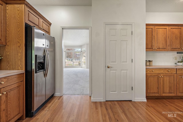 kitchen with stainless steel fridge, brown cabinetry, and light wood-style floors