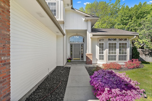 doorway to property with board and batten siding, a shingled roof, and fence