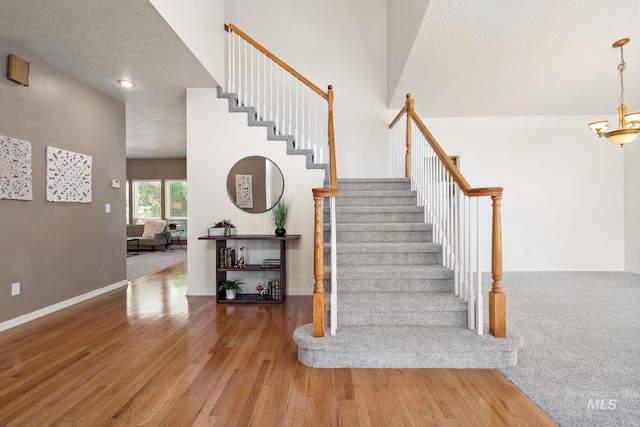 stairs featuring wood finished floors, a textured ceiling, a chandelier, and baseboards