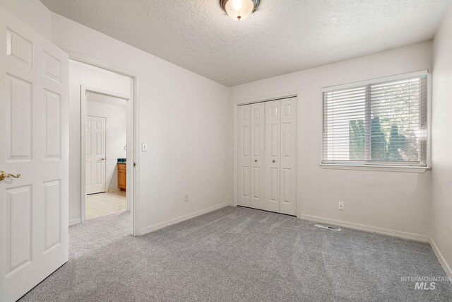 unfurnished bedroom featuring carpet, a textured ceiling, a closet, and baseboards