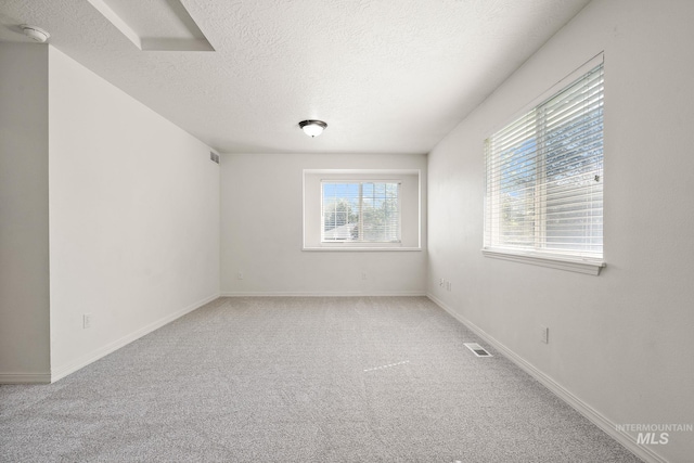carpeted spare room featuring a textured ceiling, a smoke detector, and baseboards