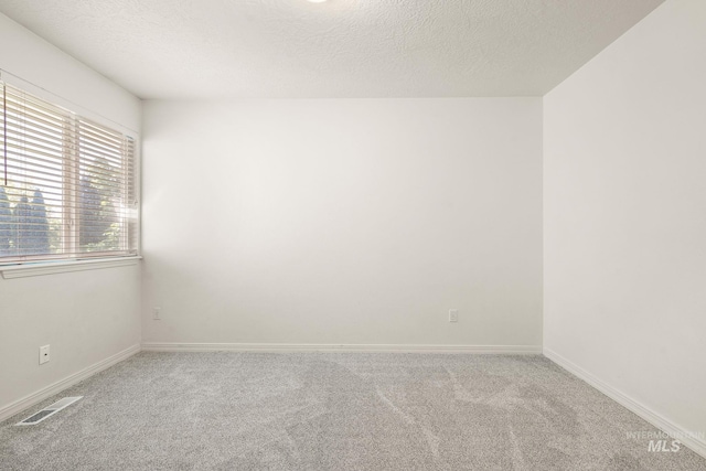 empty room with carpet, baseboards, and a textured ceiling