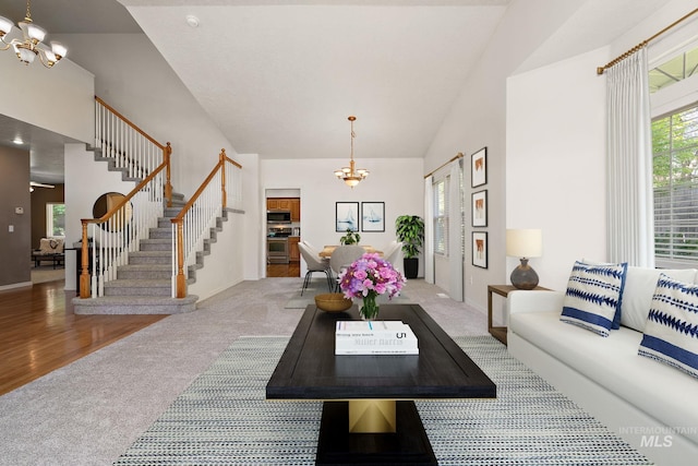 carpeted living room with a chandelier, stairway, high vaulted ceiling, and baseboards