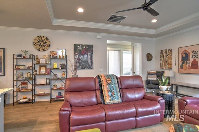 living room featuring ceiling fan, a raised ceiling, hardwood / wood-style floors, and ornamental molding