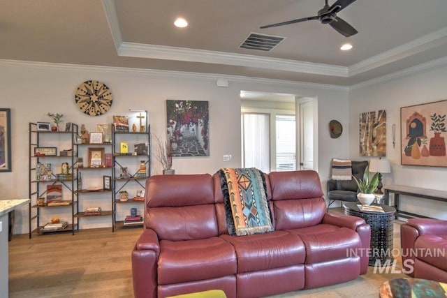 living room featuring wood finished floors, visible vents, a ceiling fan, ornamental molding, and a tray ceiling