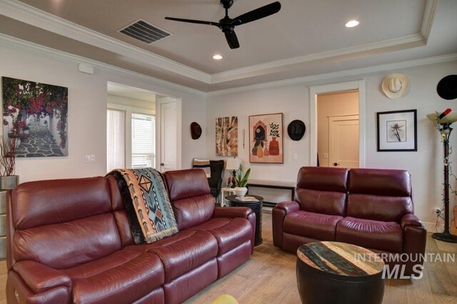 living room with ceiling fan, a raised ceiling, light hardwood / wood-style floors, and crown molding