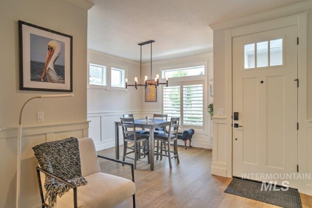 entrance foyer with light wood-type flooring, a textured ceiling, an inviting chandelier, and crown molding