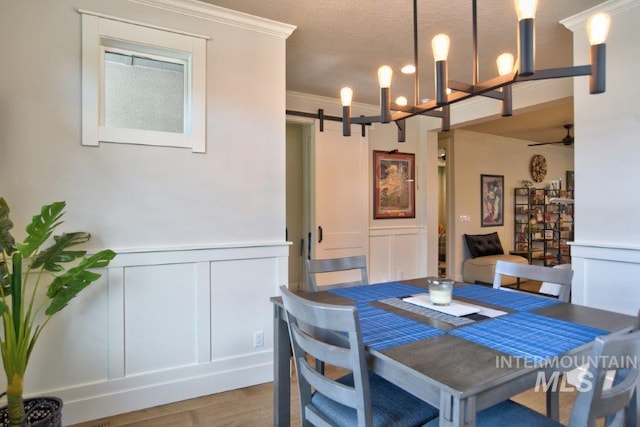 dining room featuring a barn door, ornamental molding, a decorative wall, and wood finished floors