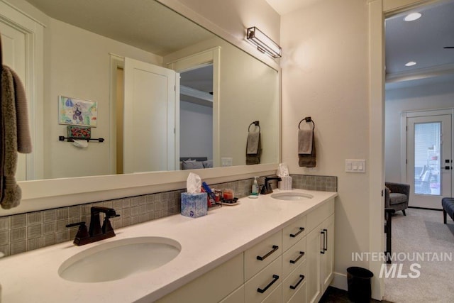 full bath with a sink, double vanity, backsplash, and ensuite bath