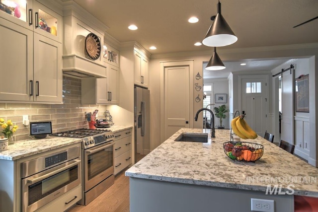 kitchen with a barn door, a sink, ornamental molding, appliances with stainless steel finishes, and a center island with sink