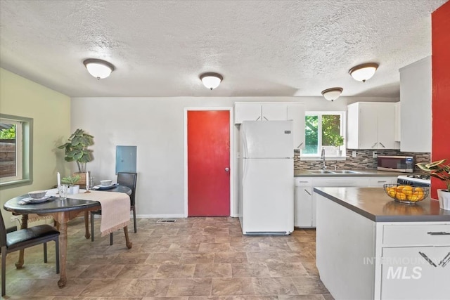 1325 E 5th N, Mountain Home, ID 83647 - kitchen featuring freestanding refrigerator, stainless steel microwave, a sink, white cabinets, and tasteful backsplash