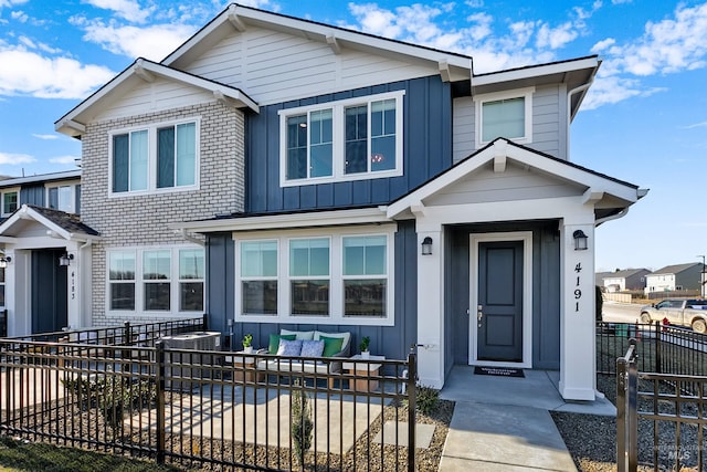 view of front of home with board and batten siding, brick siding, fence, and an outdoor living space