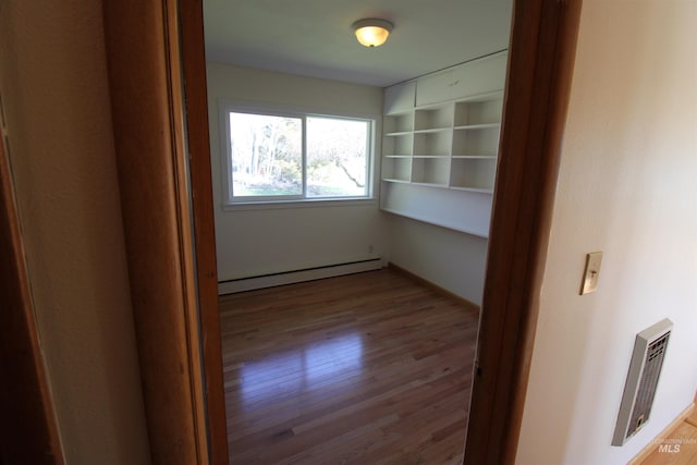 empty room with baseboard heating, visible vents, and wood finished floors