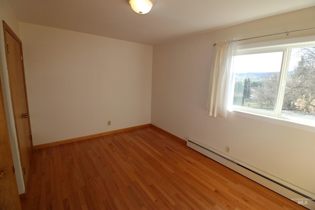 empty room featuring baseboards, light wood-type flooring, and a baseboard heating unit