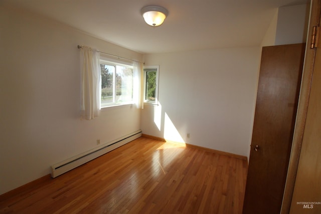 empty room with baseboard heating, light wood-type flooring, and baseboards