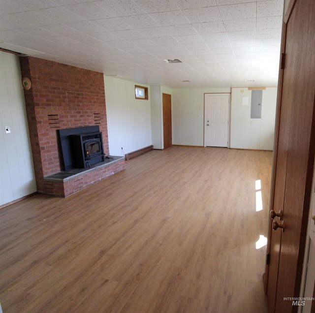 unfurnished living room with electric panel, a wood stove, light wood-style floors, and baseboards