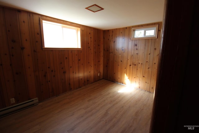 unfurnished room featuring wood walls, a baseboard heating unit, and wood finished floors