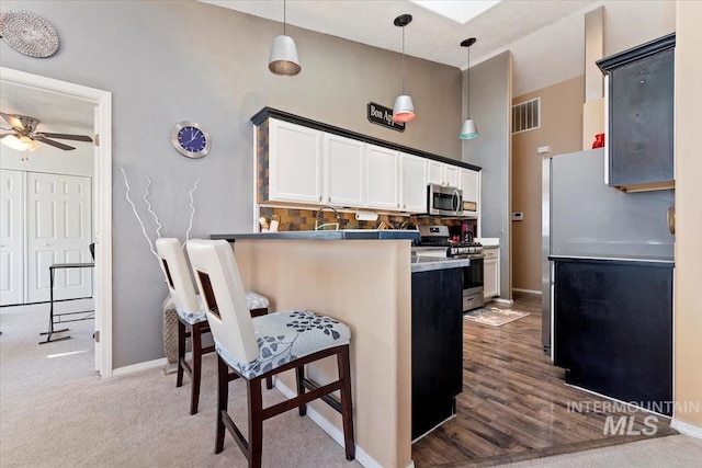 kitchen featuring a breakfast bar area, white cabinetry, kitchen peninsula, pendant lighting, and stainless steel appliances