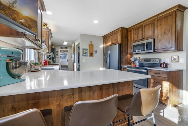 kitchen featuring hardwood / wood-style flooring, a kitchen breakfast bar, kitchen peninsula, and appliances with stainless steel finishes