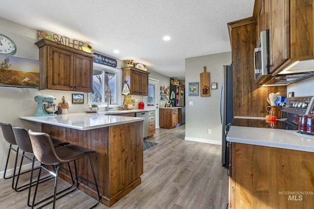 kitchen featuring a breakfast bar, light wood-type flooring, a textured ceiling, kitchen peninsula, and stainless steel appliances