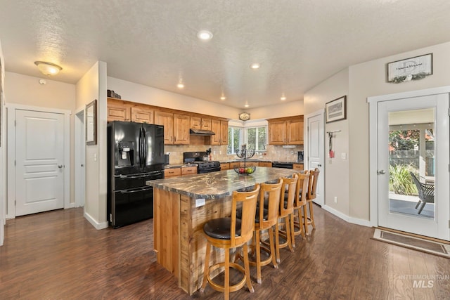 kitchen with tasteful backsplash, a breakfast bar, dark hardwood / wood-style floors, black appliances, and a center island