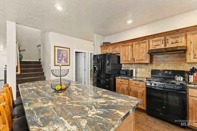 kitchen featuring black appliances, a center island, dark hardwood / wood-style flooring, dark stone counters, and a breakfast bar