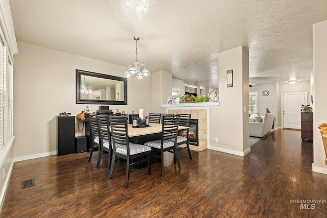 dining room with a tile fireplace, a textured ceiling, dark hardwood / wood-style floors, and a chandelier