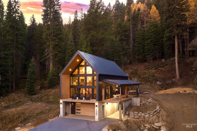 view of front of home featuring an attached garage, a view of trees, driveway, and metal roof