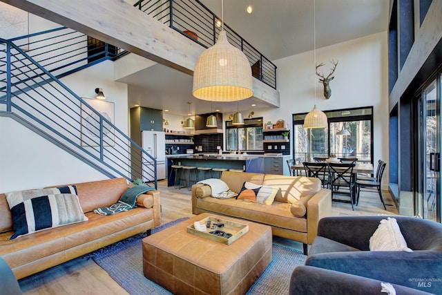 living area with stairway, light wood-style floors, and a high ceiling