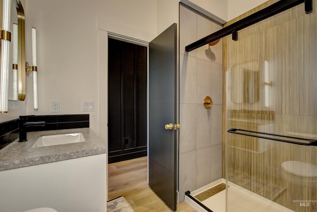 full bath with toilet, a stall shower, vanity, and wood finished floors