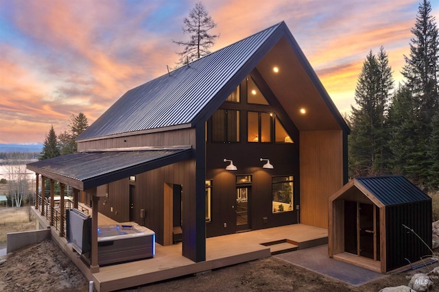 back of house at dusk featuring an outbuilding, a wooden deck, metal roof, and a hot tub