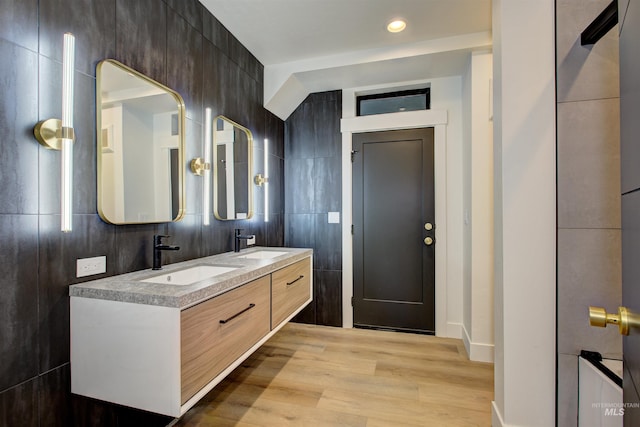 bathroom with tile walls, wood finished floors, double vanity, and a sink