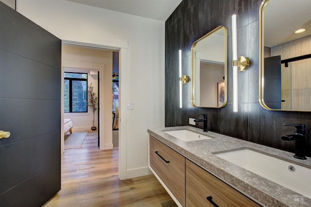 ensuite bathroom with double vanity, wood finished floors, baseboards, and a sink