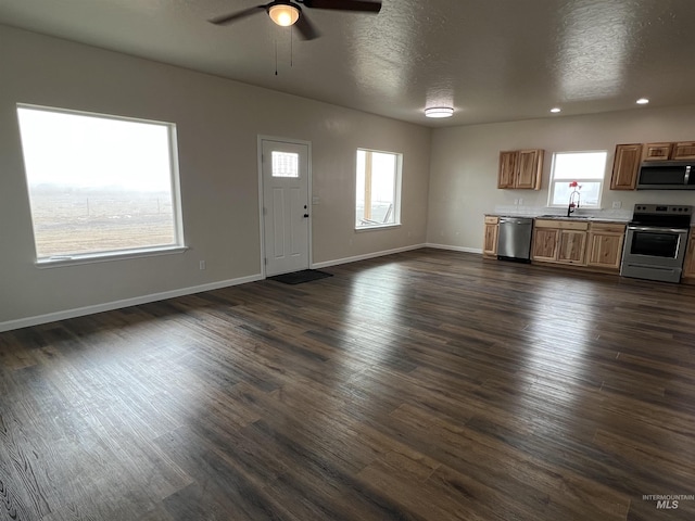 kitchen with stainless steel appliances, a sink, open floor plan, light countertops, and dark wood finished floors