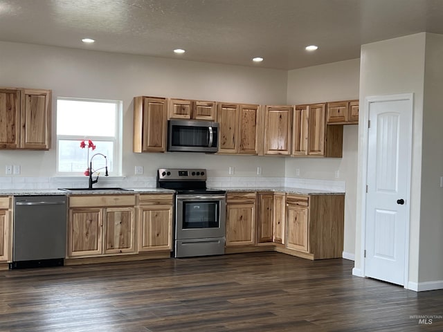 kitchen with dark wood-style flooring, recessed lighting, appliances with stainless steel finishes, a sink, and light stone countertops