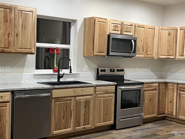 kitchen with stainless steel appliances, dark wood-style flooring, a sink, and light stone countertops