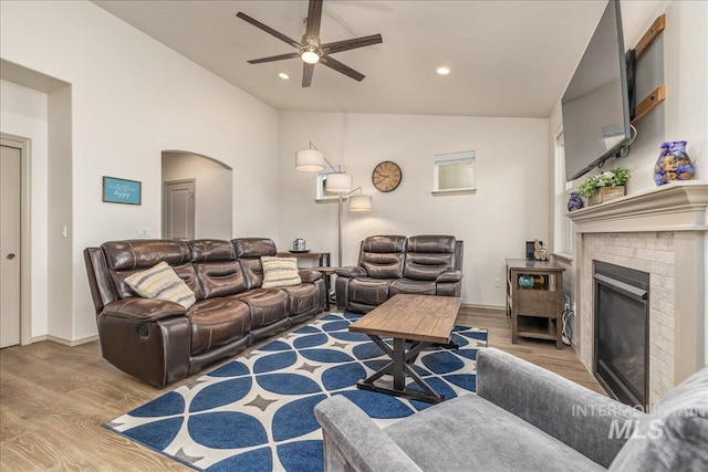 7566 W Corona Dr, Boise, ID 83709 - living room with vaulted ceiling, wood finished floors, a ceiling fan, arched walkways, and a brick fireplace