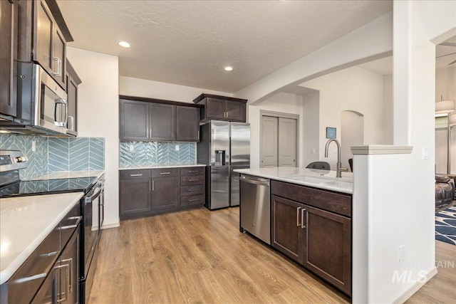 7566 W Corona Dr, Boise, ID 83709 - kitchen with stainless steel appliances, a sink, arched walkways, dark brown cabinets, and light wood-style flooring