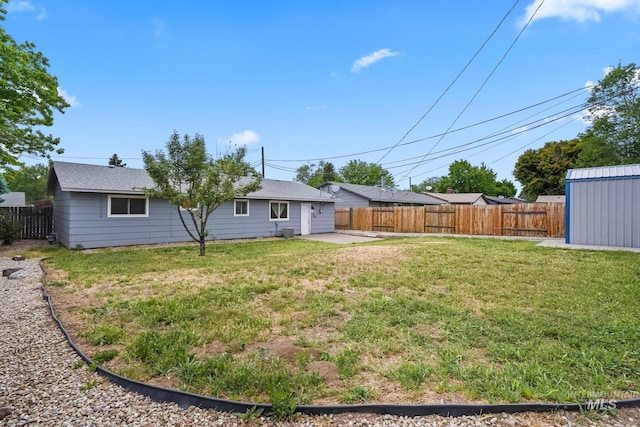 rear view of property featuring a storage unit, a fenced backyard, a lawn, and an outbuilding