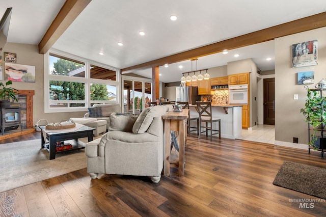 living room featuring beamed ceiling, light wood-type flooring, a wood stove, and sink