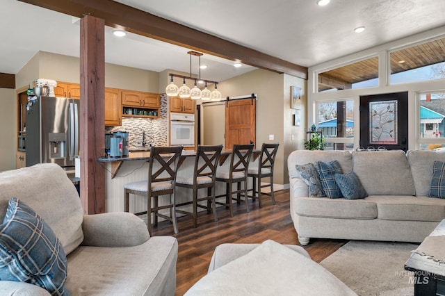 living room with a barn door, dark hardwood / wood-style flooring, lofted ceiling with beams, and sink