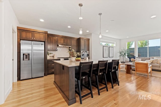 kitchen featuring dark brown cabinetry, light wood-style floors, stainless steel fridge, light countertops, and under cabinet range hood