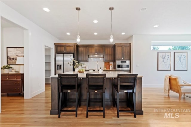 kitchen with light countertops, stainless steel appliances, a center island with sink, and light wood-style flooring