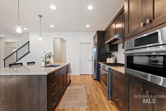 kitchen featuring dark brown cabinetry, a sink, an island with sink, stainless steel appliances, and under cabinet range hood