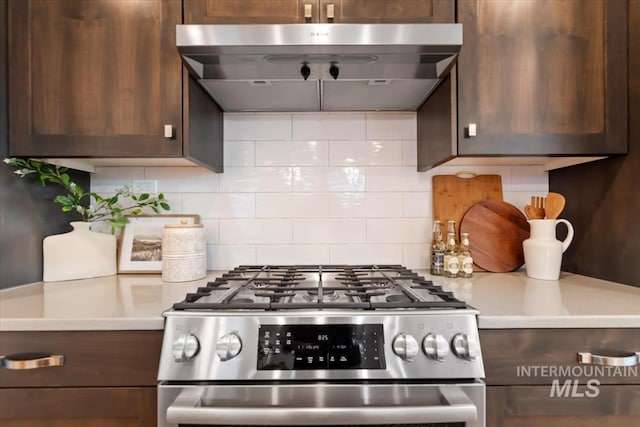 kitchen with wall chimney range hood, backsplash, gas range, dark brown cabinets, and light countertops
