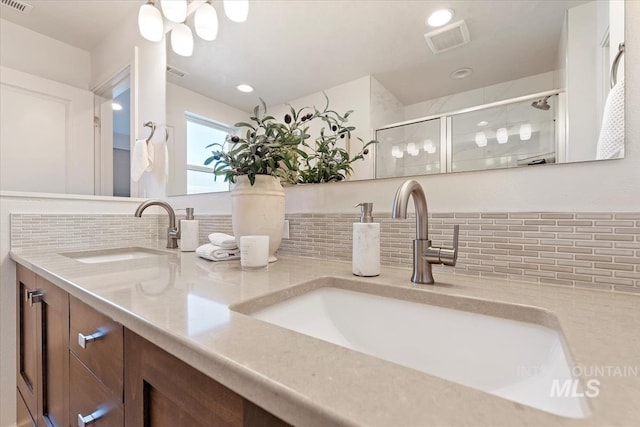 full bath with visible vents, a sink, a shower stall, and tasteful backsplash