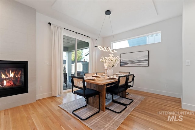dining room with baseboards, a tiled fireplace, and wood finished floors