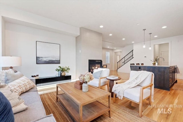 living area with recessed lighting, light wood-style flooring, a fireplace, and stairway