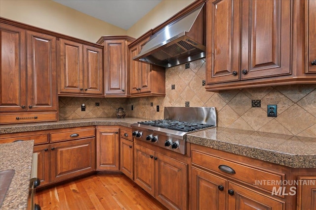 kitchen with light wood-type flooring, stainless steel gas cooktop, wall chimney range hood, and tasteful backsplash